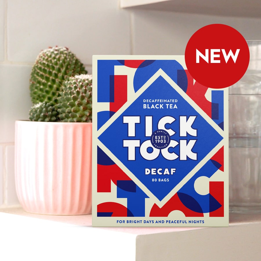 A red, white and blue box of Tick Tock Decaf Black Tea on a white shelf with a potted cactus to one side and a stack of glass tumblers to the other.
